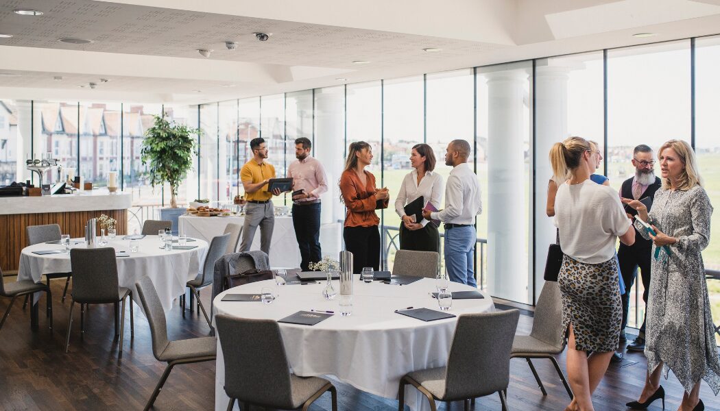 People standing in a room. Tables decorated. People chatting